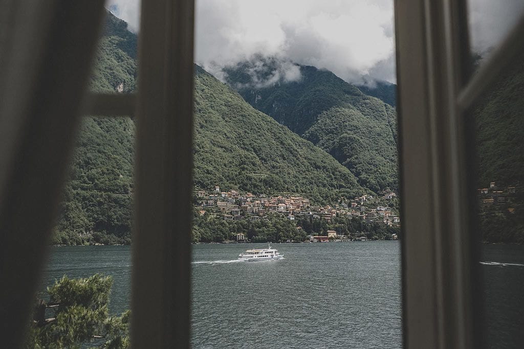 A view of a lake with a boat, surrounded by lush green hills and a town in the background.