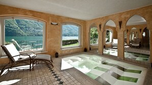 Un cuarto de spa con una bañera grande, una silla de descanso y vistas a un lago y montañas.