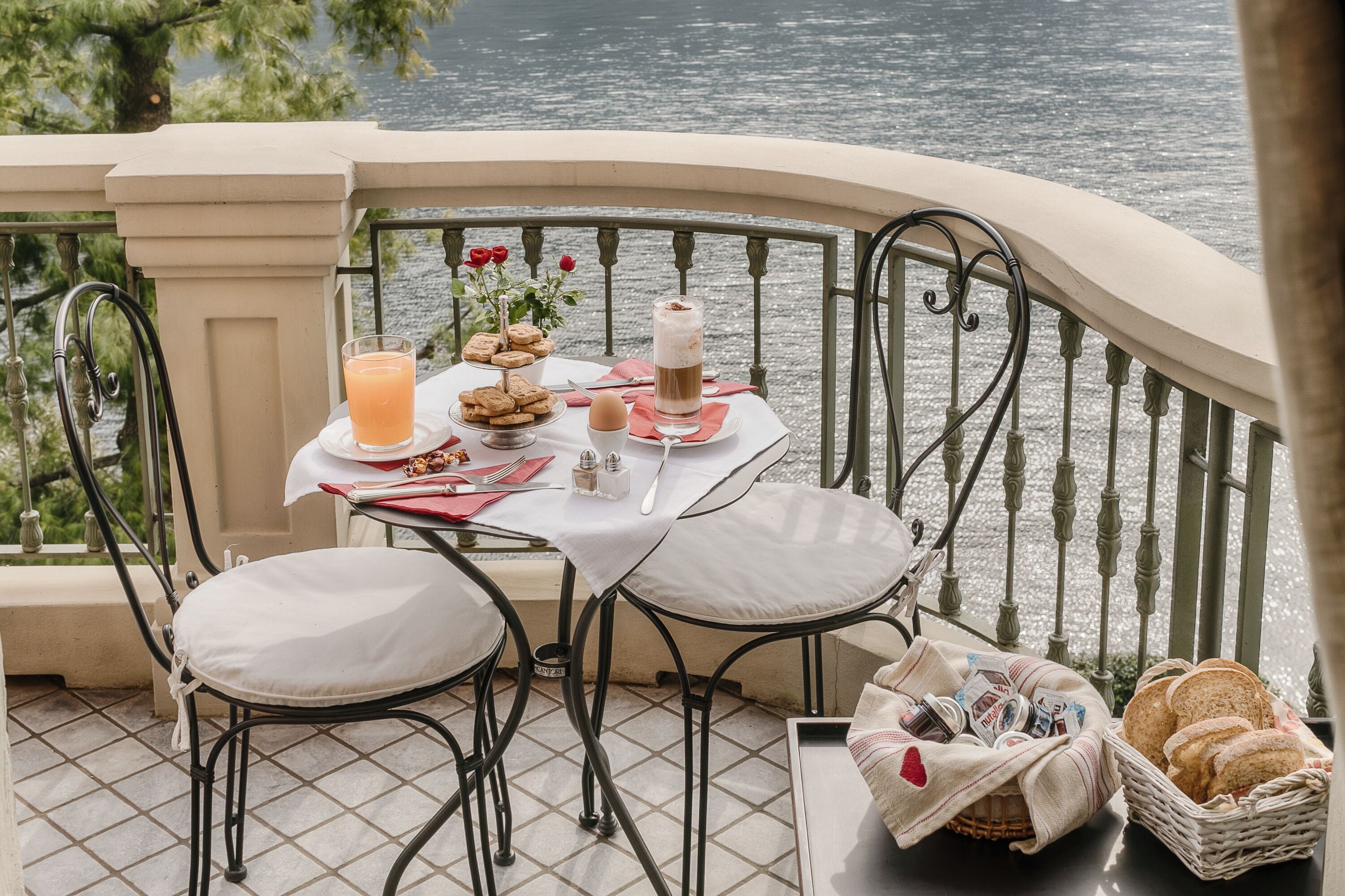 A dining table with a glass of orange juice, cookies, and a cup of coffee on a balcony overlooking a body of water.
