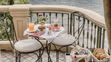 A dining table with a glass of orange juice, cookies, and a cup of coffee on a balcony overlooking a body of water.