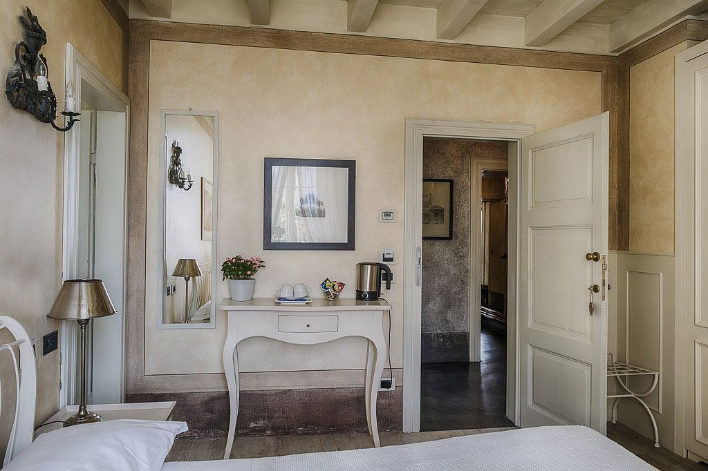 Une chambre à coucher comprenant un lit, un bureau avec une chaise, une lampe, un miroir et une porte donnant sur une autre pièce.