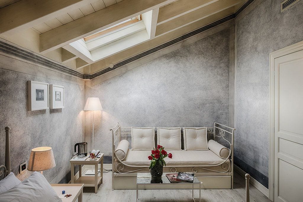 A cozy room with a sofa, a table with a vase of flowers, a lamp, and framed pictures on the wall.