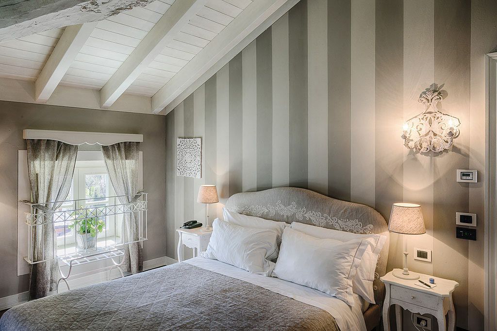Une chambre à coucher avec un grand lit, une table de chevet avec une lampe, un luminaire fixé au mur et une fenêtre avec des rideaux.
