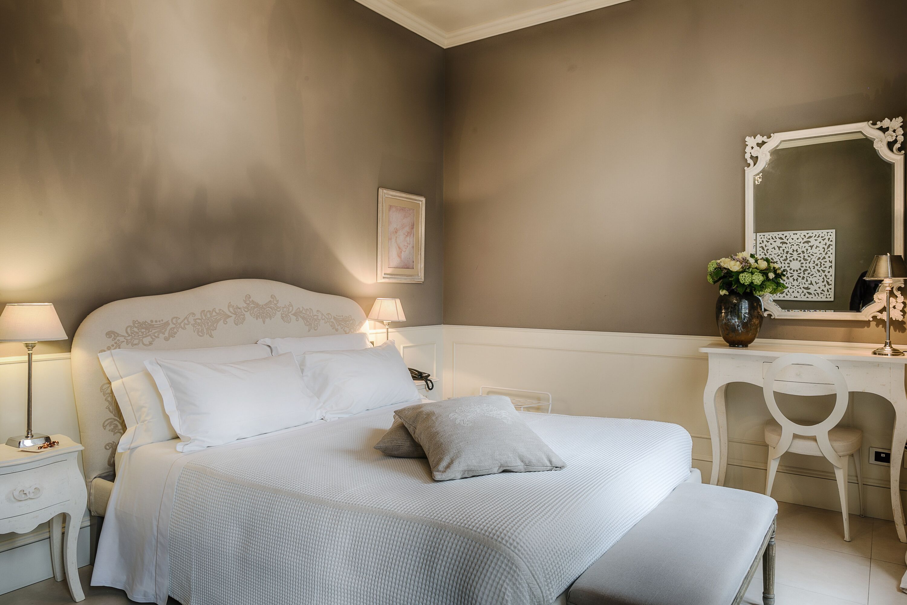 A bedroom with a large bed, bedside tables, a vanity with a mirror, and a chair.
