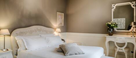 A bedroom with a large bed, bedside tables, a vanity with a mirror, and a chair.