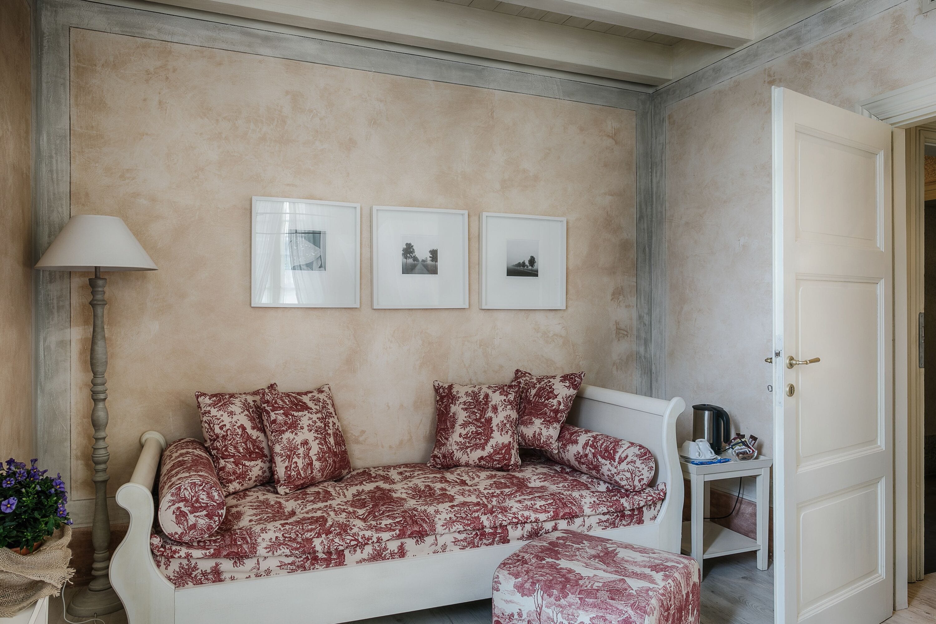 Ein Zimmer mit einer Couch, einer Lampe, einem kleinen Tisch mit Wasserkocher und drei gerahmten Bildern an der Wand.