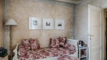 Ein Zimmer mit einer Couch, einer Lampe, einem kleinen Tisch mit Wasserkocher und drei gerahmten Bildern an der Wand.