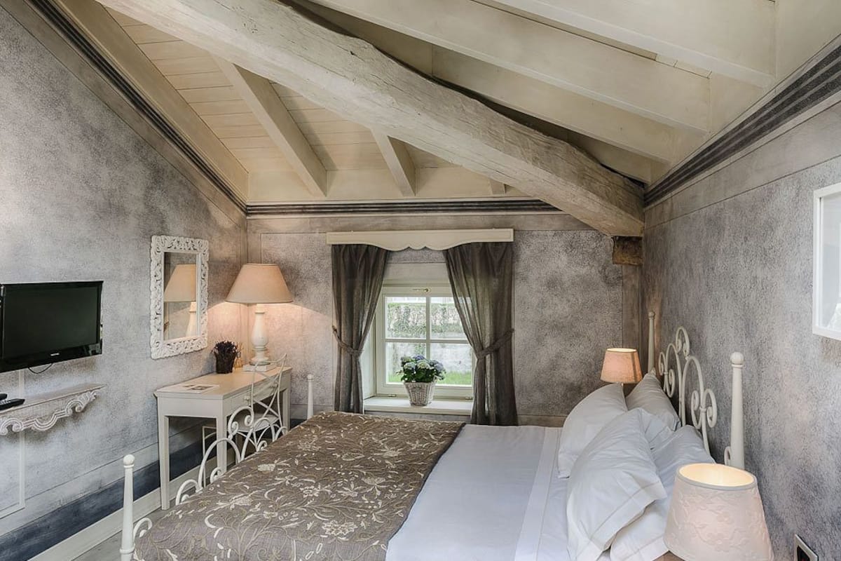 A bedroom with a bed, bedside lamps, a television, a desk, and a window with curtains.