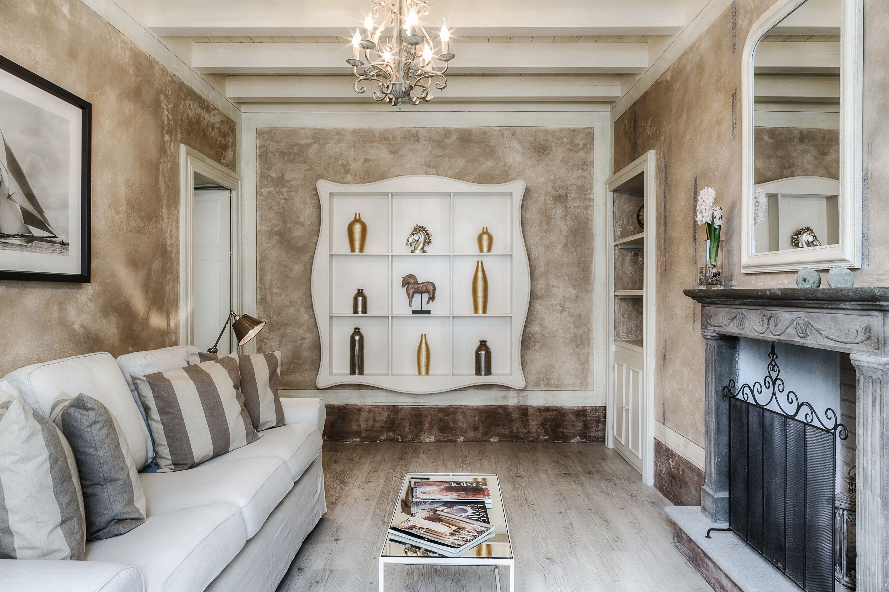 A living room with a white sofa, a coffee table with magazines, a decorative shelf with vases, and a fireplace.