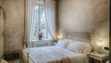 Ein Schlafzimmer mit einem Bett, einem Nachttisch, einer Lampe, einem Fenster mit Vorhängen und einer Deckenleuchte.