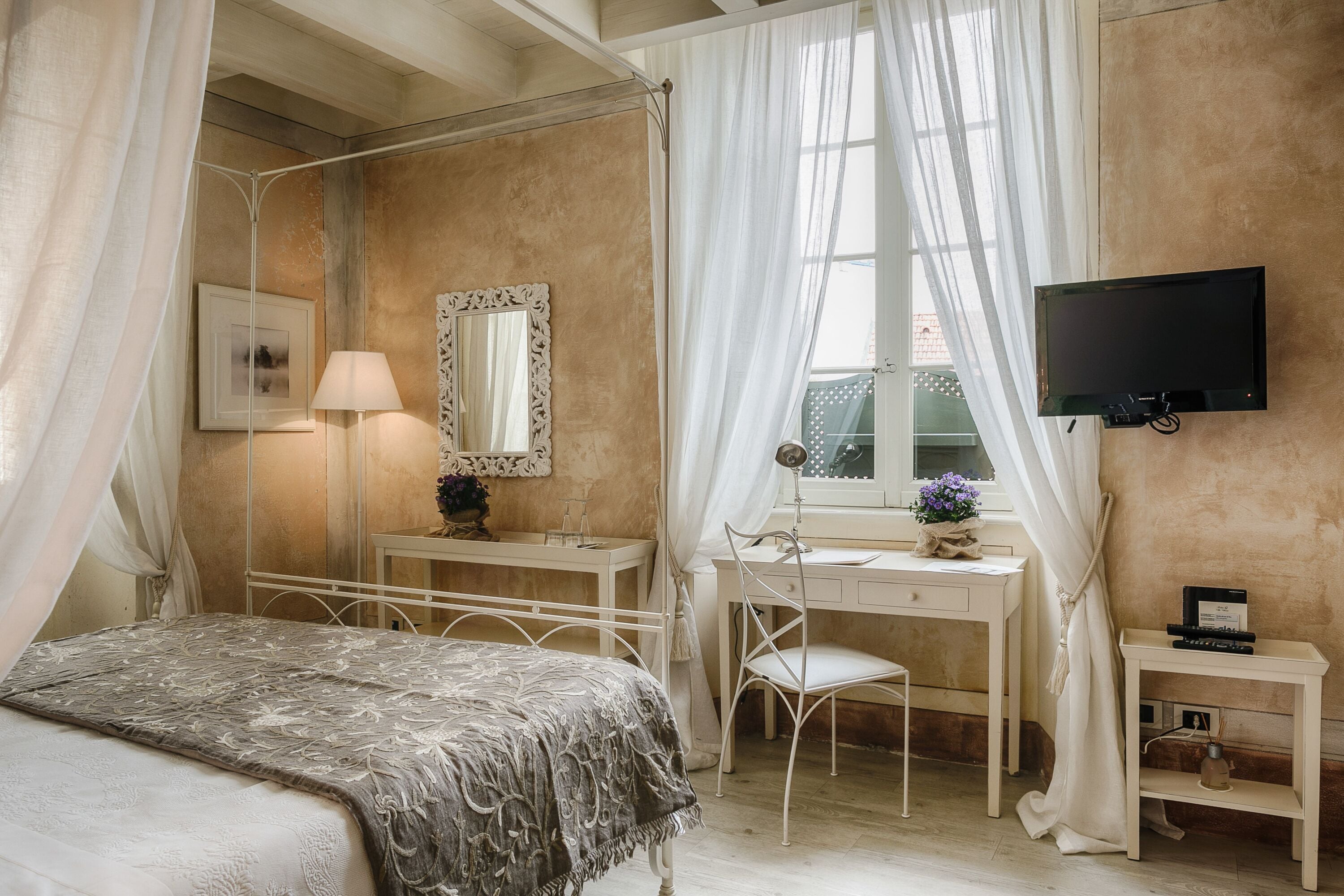 Een slaapkamer met een bed, een bureau, een stoel, een televisie en een raam met gordijnen.