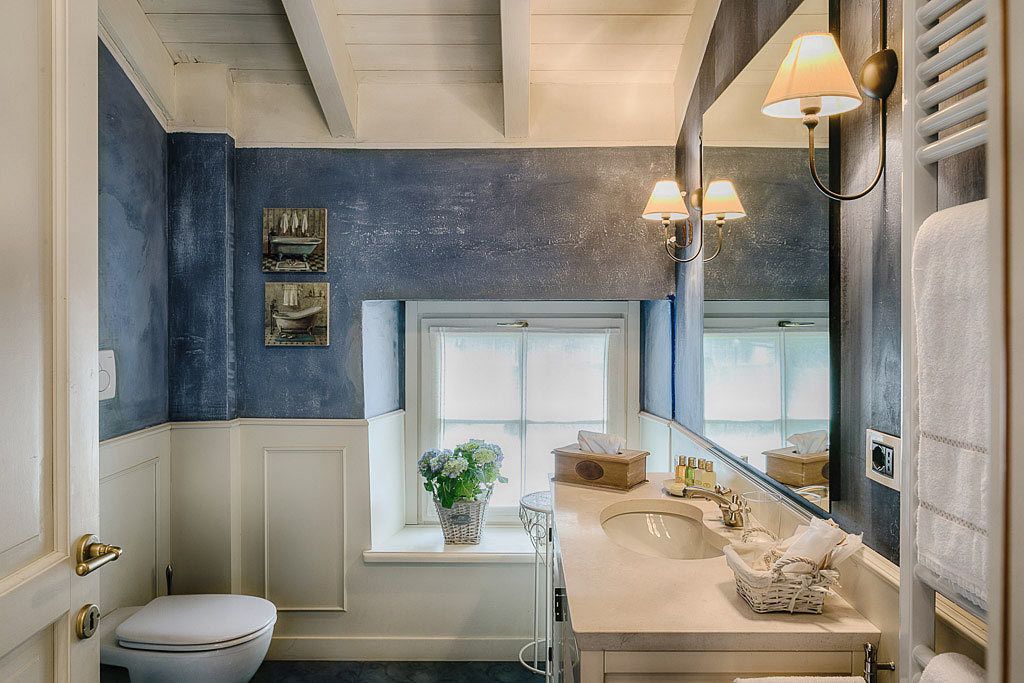 Un baño con inodoro blanco, lavamanos con espejo y ventana con vistas.