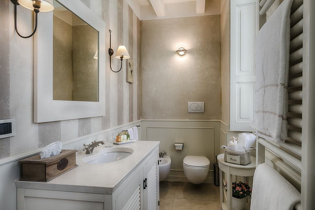 A bathroom with two sinks, a toilet, and a bidet. There are wall sconces and a mirror above the sinks.