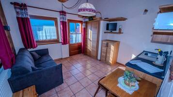 A compact living space with a sofa, a dining table, a television, and a kitchenette area.