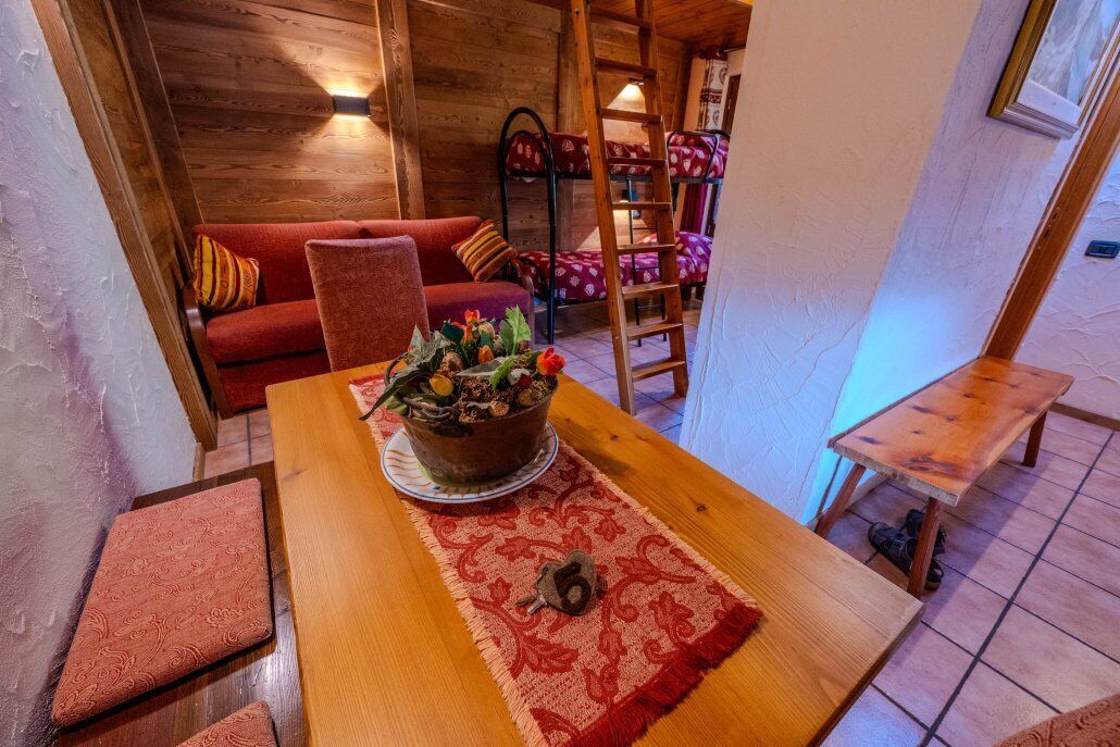 Um quarto acolhedor com uma mesa de madeira, um sofá vermelho, uma cama beliche e um pequeno banco de madeira.