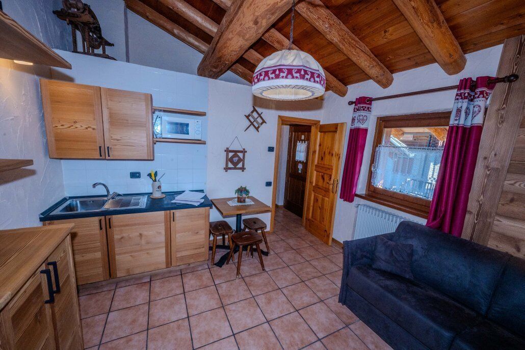 Una cocina compacta con armarios de madera, una zona de comedor con mesa y sillas, un sofá y una lámpara colgante.
