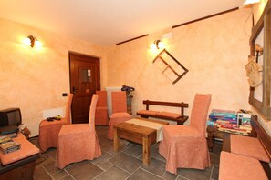 Una habitación acogedora con una mesa de madera, cuatro sillones, un televisor y un estante con libros y una caja.