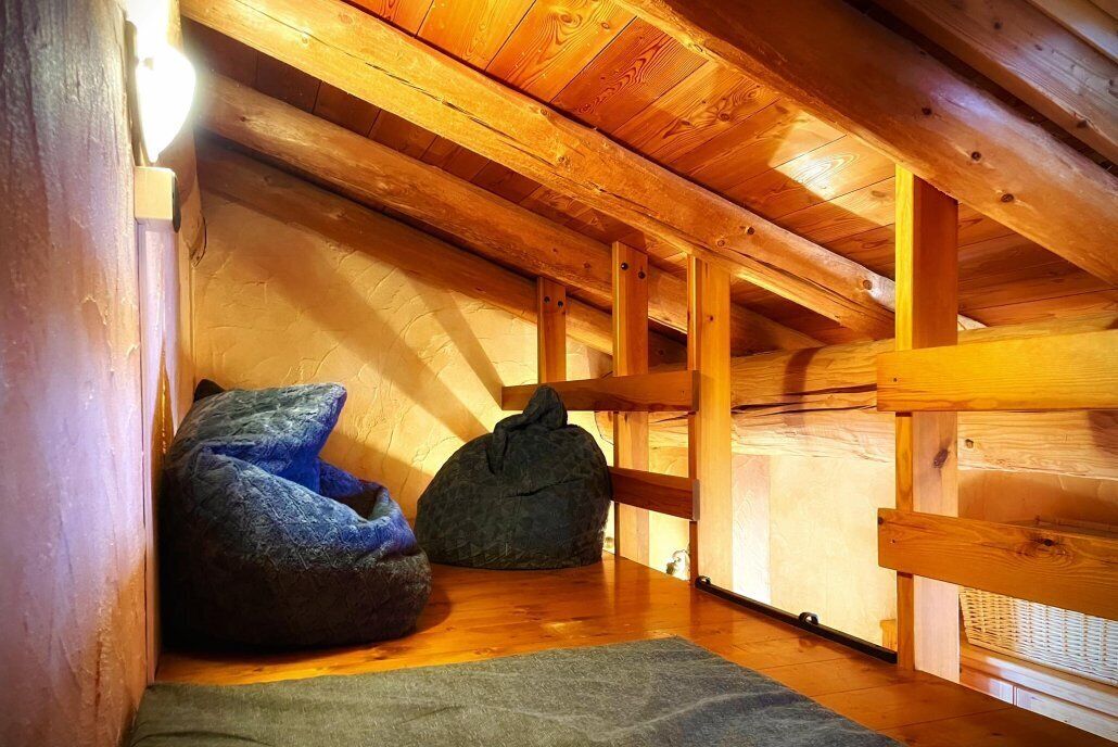Ein gemütliches Dachzimmer mit Holzbalken, einem grünen Sitzsack und einem kleinen Teppich.