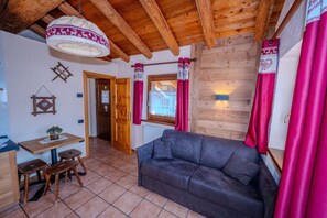 A cozy room with a wooden ceiling, a sofa, a table with stools, and a window with curtains. - Residence Trompe-L'Oeil (Ayas)