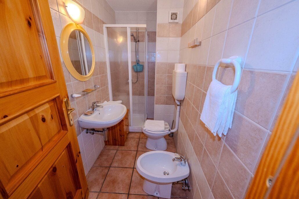 A bathroom with a wooden door, two sinks, a toilet, and a shower.
