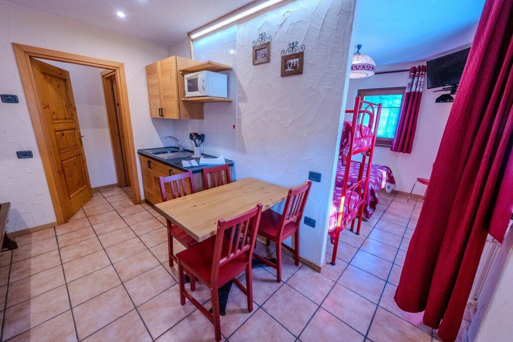 A compact kitchen with a dining area, wooden cabinets, and a red chair.