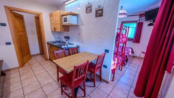 A compact kitchen with a dining area, wooden cabinets, and a red chair.