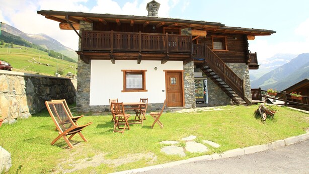 Un chalet con fachada de piedra, balcón de madera y una escalera que conduce a un nivel superior.