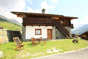 Un chalet doté d’une façade en pierre, d’un balcon en bois et d’un escalier menant à un étage supérieur.