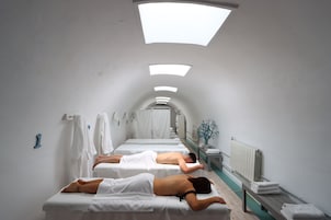 Sala de spa com duas macas de massagem, um radiador e um banco com toalhas.