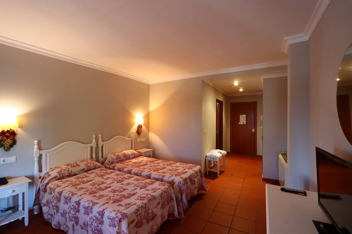 A hotel room with two beds, a desk, a chair, a TV, and a small table.