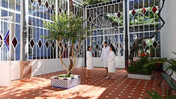 Uma área externa coberta com piso de azulejos, uma árvore central e um banco.