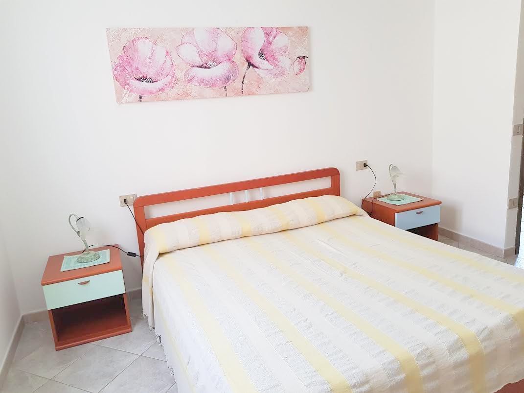 Un dormitorio con cama, mesitas de noche, lámpara y una obra de arte floral en la pared.