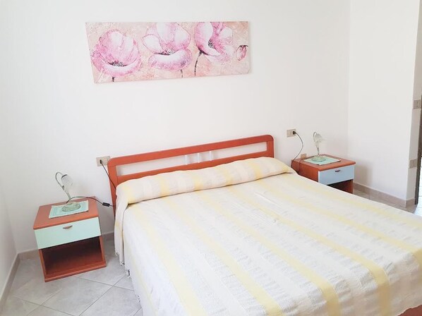 Un dormitorio con cama, mesitas de noche, lámpara y una obra de arte floral en la pared.
