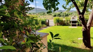 Un jardín cuidado con un banco de piedra, un sendero y vistas a colinas distantes.