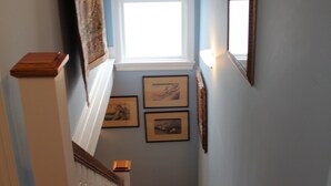 A staircase with wooden steps and white railings, leading to a landing with a window and framed pictures on the wall. - Rising Sun Bed & Breakfast (Natchez)