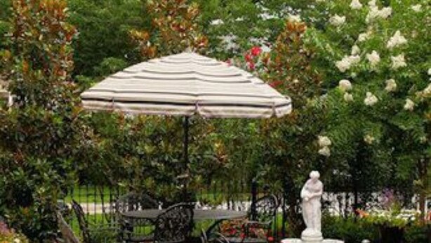 An outdoor patio with a brick floor, a white umbrella, and black metal chairs. - Rising Sun Bed & Breakfast (Natchez)