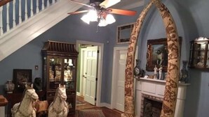 A hallway with a wooden floor, a decorative horse sculpture, a fireplace, and a ceiling fan. - Rising Sun Bed & Breakfast (Natchez)