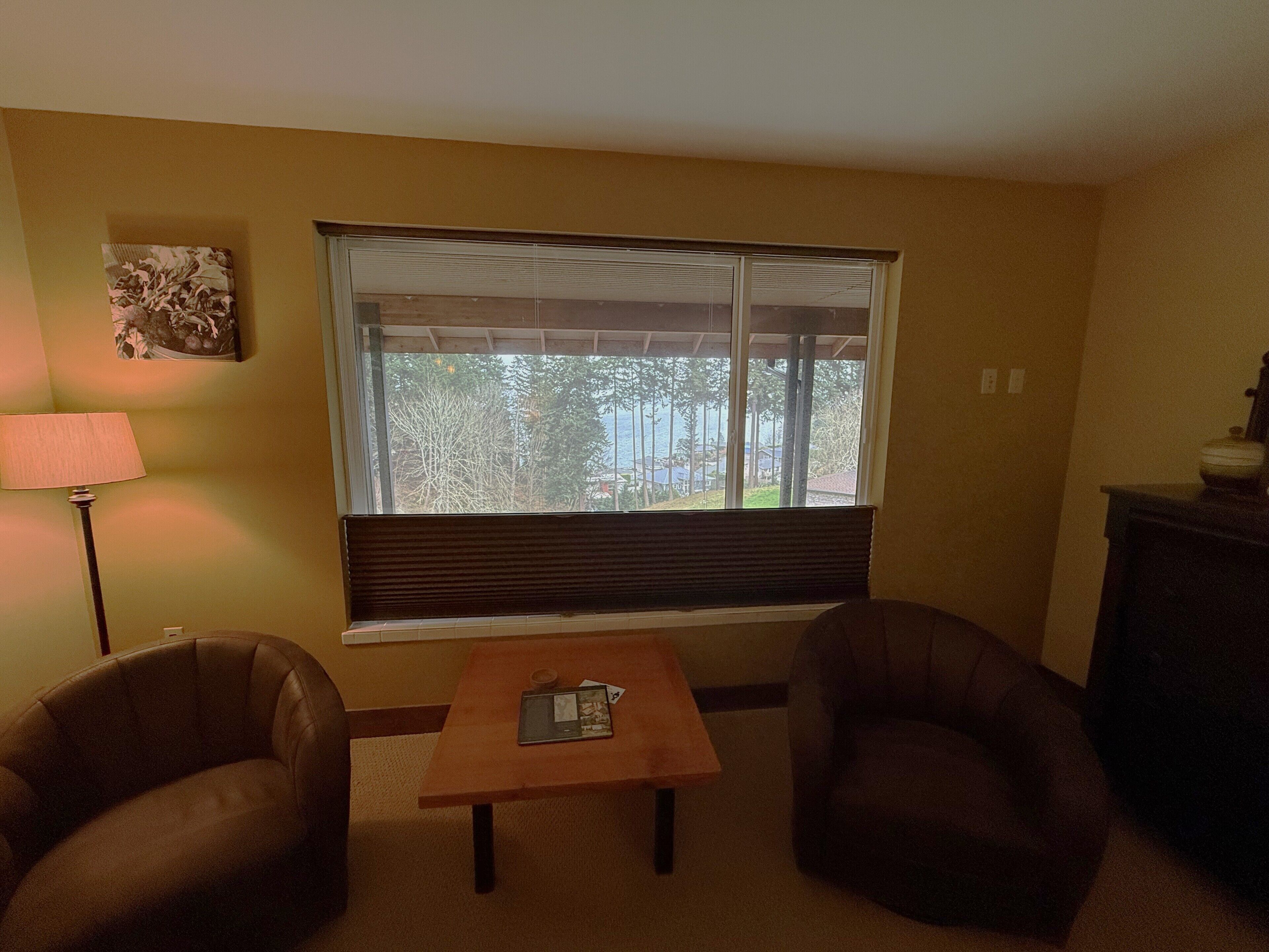 Ein Wohnzimmer mit großem Fenster, einer Lampe, zwei Sesseln und einem kleinen Tisch.