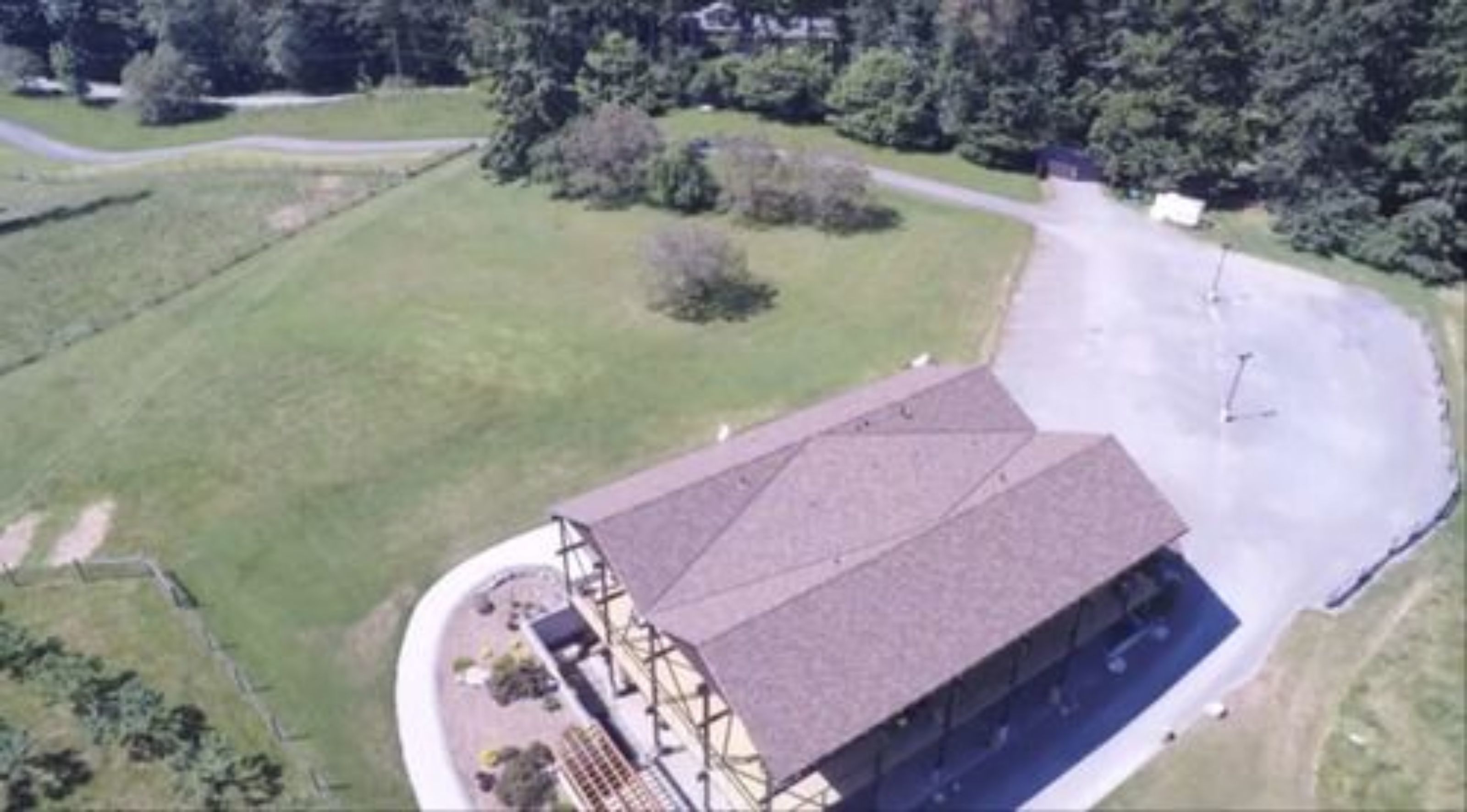 An aerial view of a building with a large parking area and a green field.
