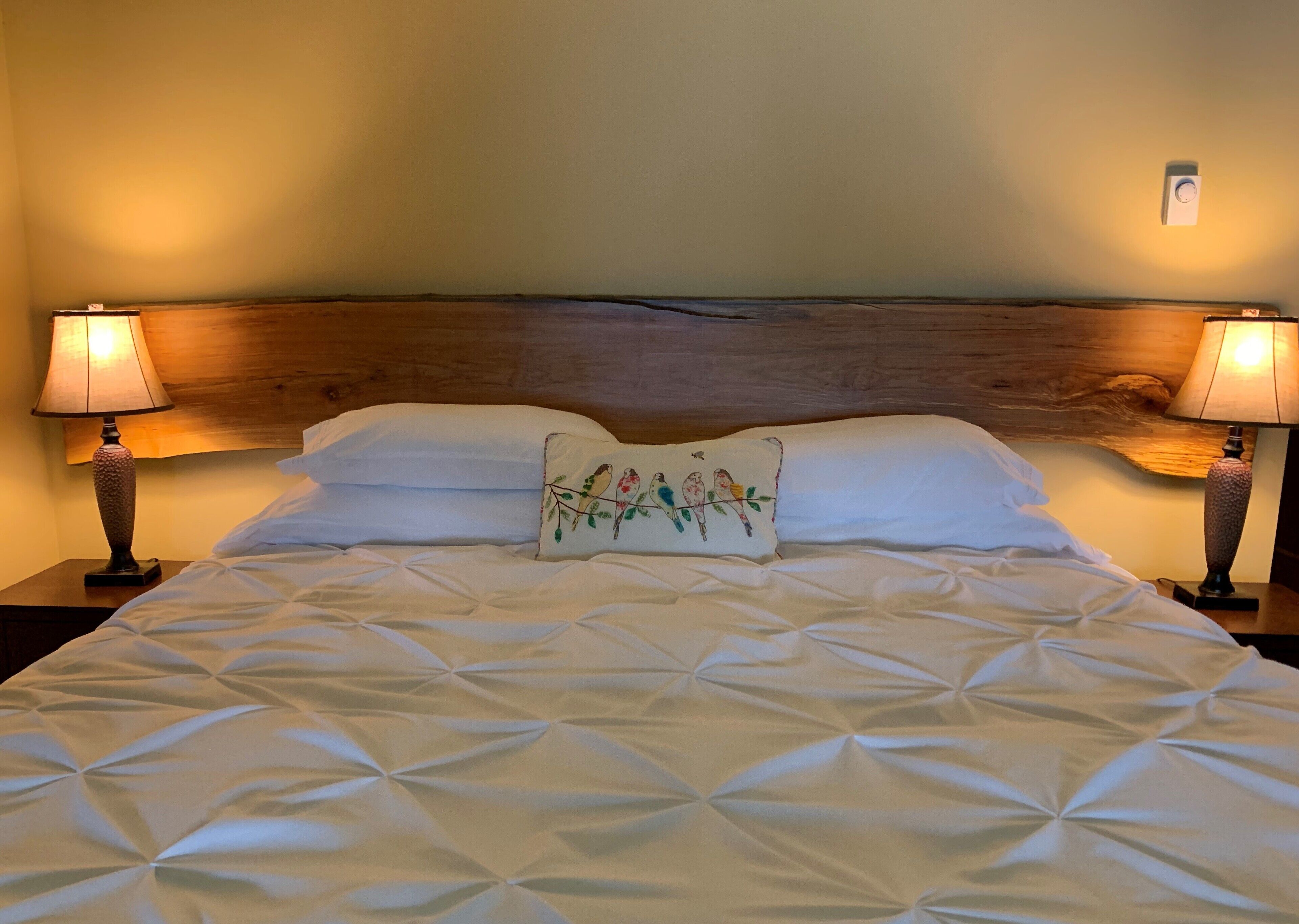 A neatly made bed with a geometric patterned bedspread, flanked by two bedside lamps and a wooden headboard.