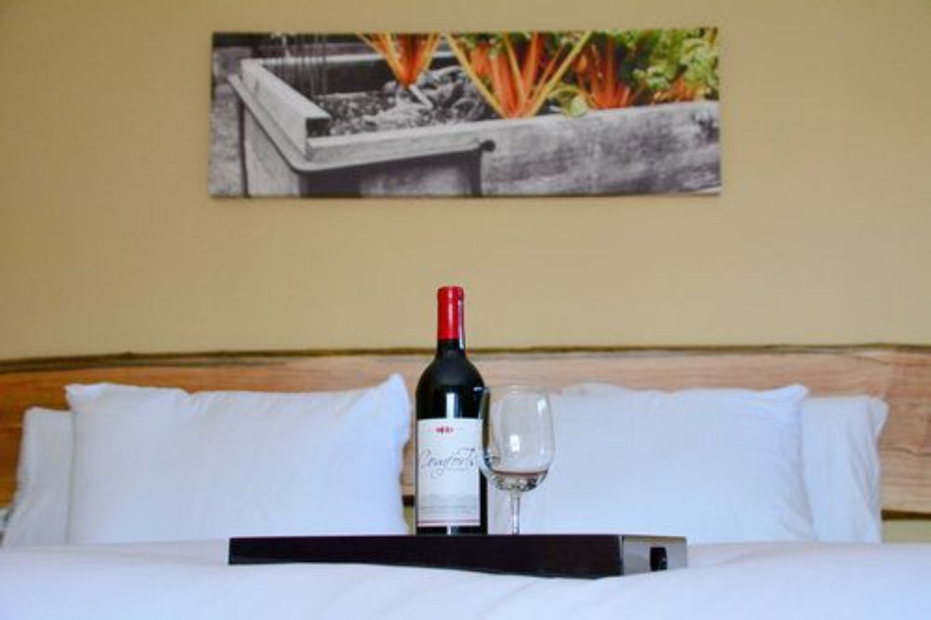 Ein Hotelzimmer mit einem Bett, weißen Kissen, einer Weinflasche und einem Glas auf einem Tablett.