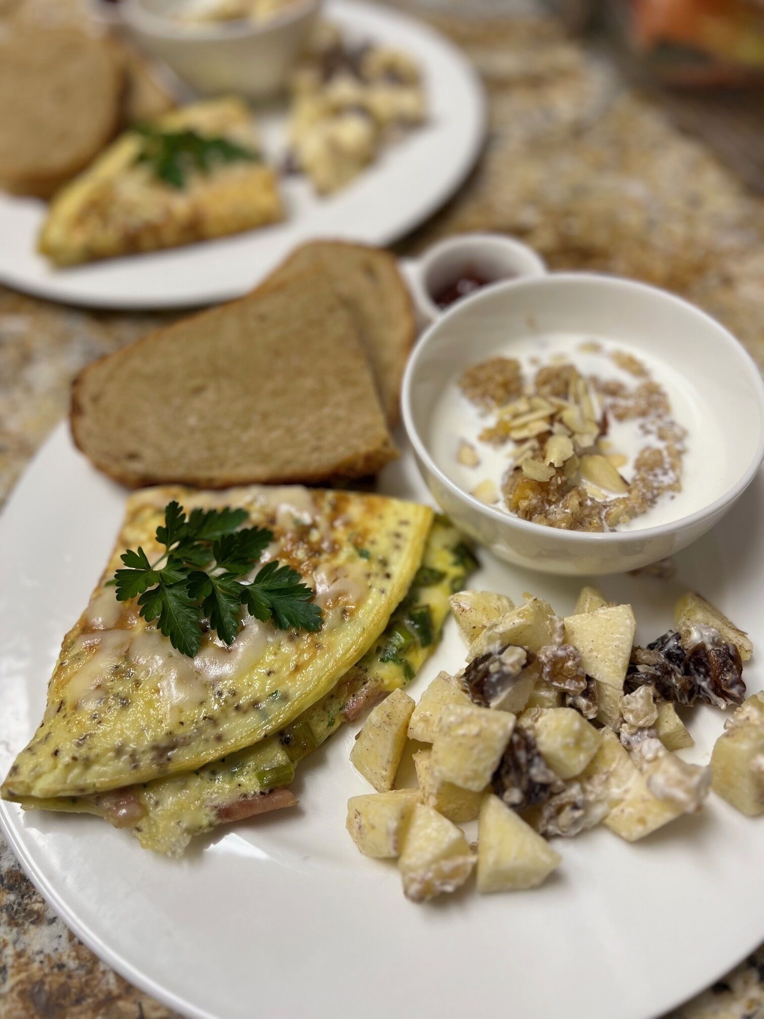 A breakfast plate with toast, scrambled eggs, potatoes, and a bowl of yogurt with nuts.