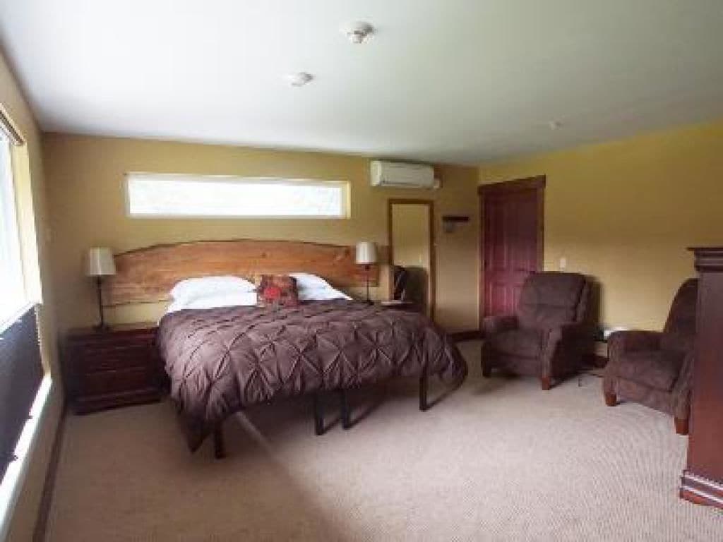 A bedroom with a bed, two chairs, a dresser, and a window.