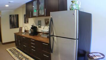 A kitchen with dark wooden cabinets, a stainless steel refrigerator, a coffee maker, and a patterned rug.