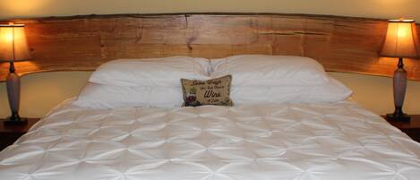 Un lit bien fait, recouvert d’une courtepointe, avec deux lampes de chevet et un coussin décoratif orné d’une citation.