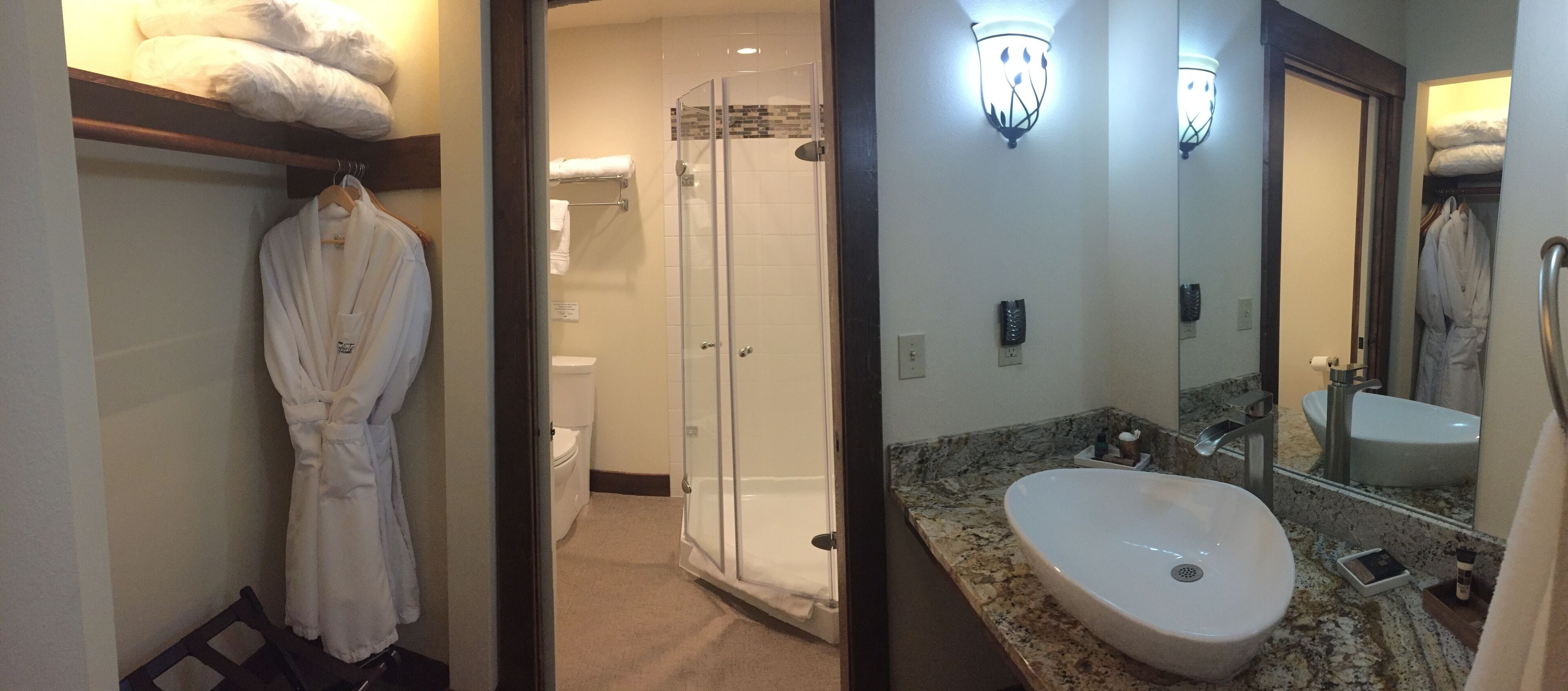 Une salle de bain d’hôtel avec une douche à l’italienne, un grand miroir et un peignoir suspendu à un porte-serviettes.