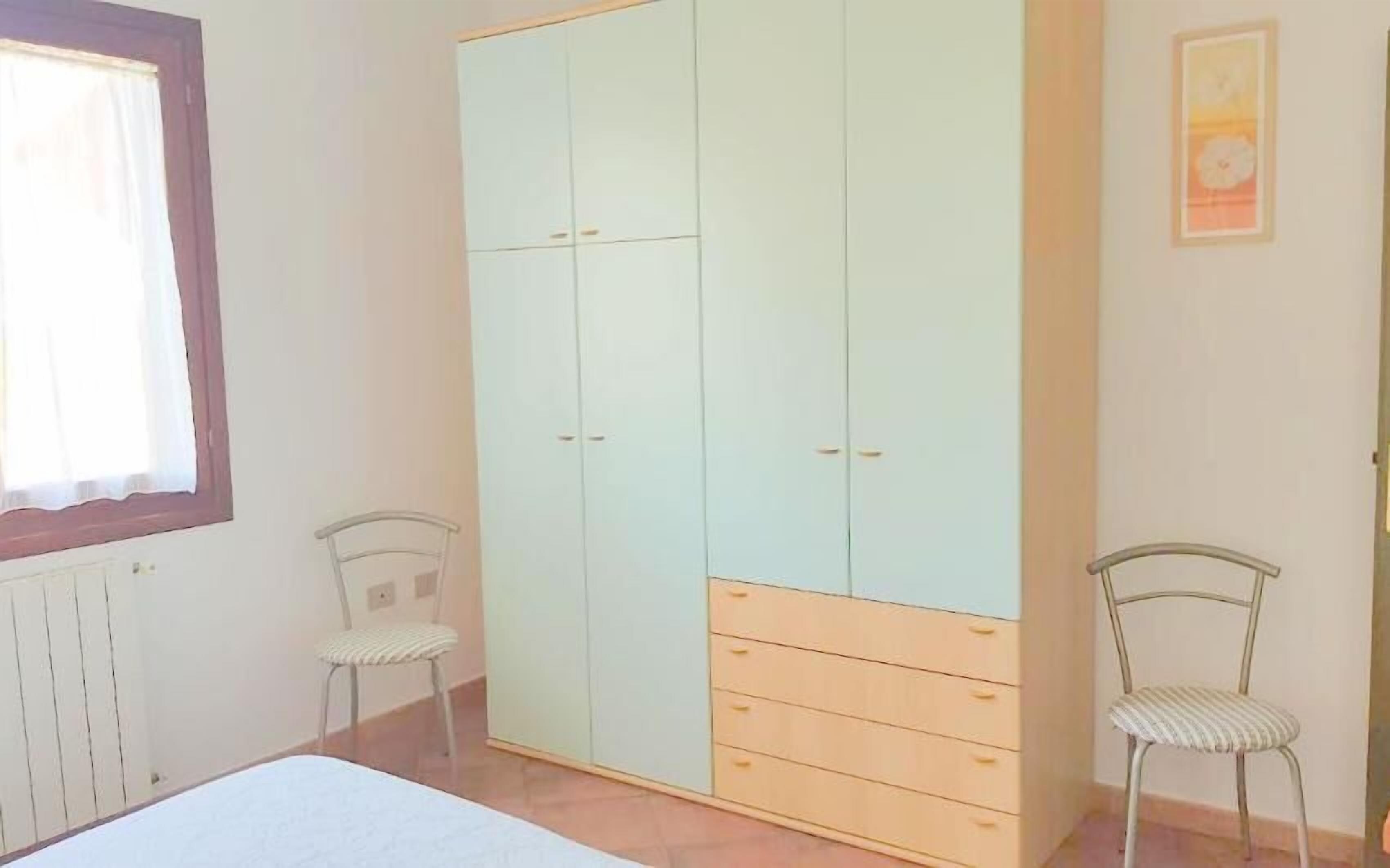 A bedroom with a bed, a wardrobe, two chairs, and a radiator.