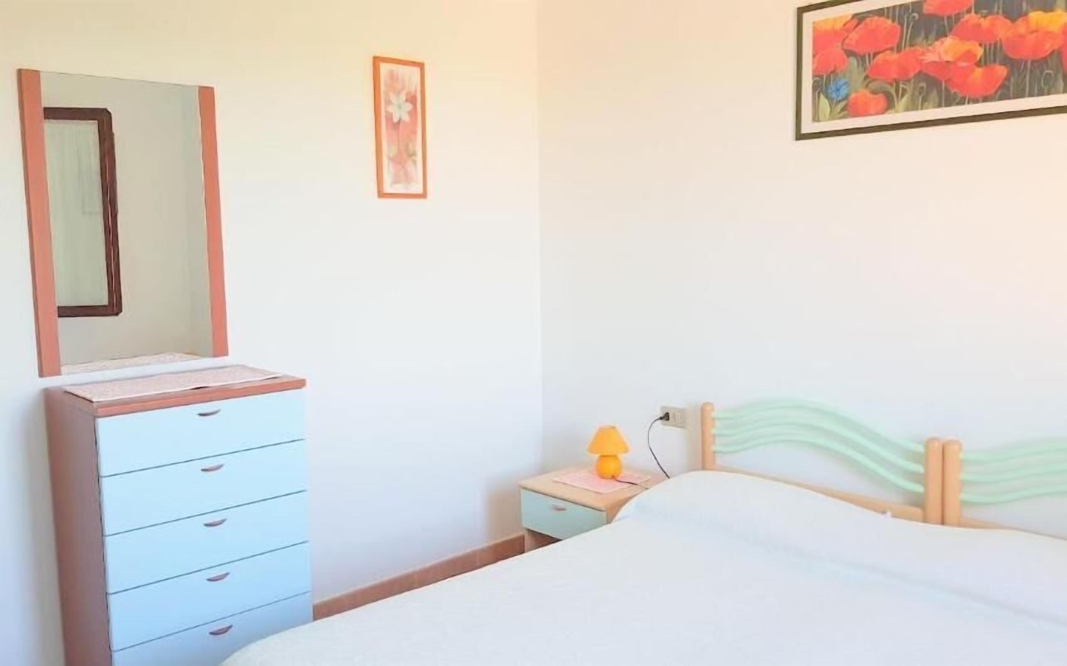 Un dormitorio con cama, cómoda, mesita de noche, lámpara y dos cuadros en la pared.