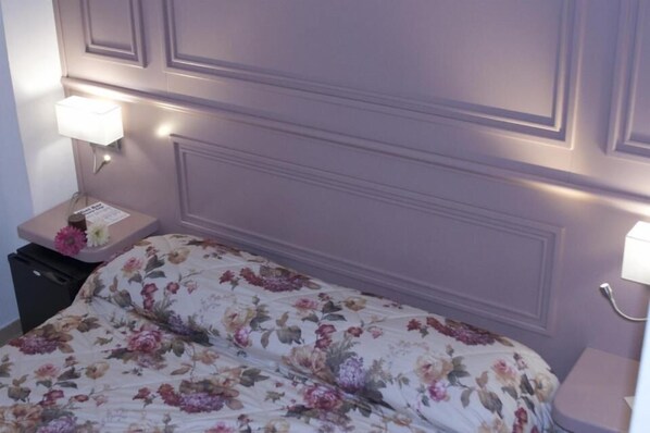 Un dormitorio con colcha estampada, cabecera con paneles y lámparas de noche.
