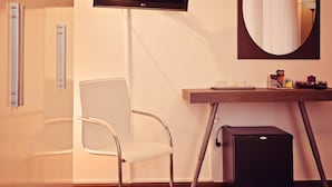 A modern hotel room with a flat-screen TV mounted on the wall, a round mirror, a wooden desk with a cup and a small bowl, and a compact black speaker. - B&B Sul Corso (Salerno)